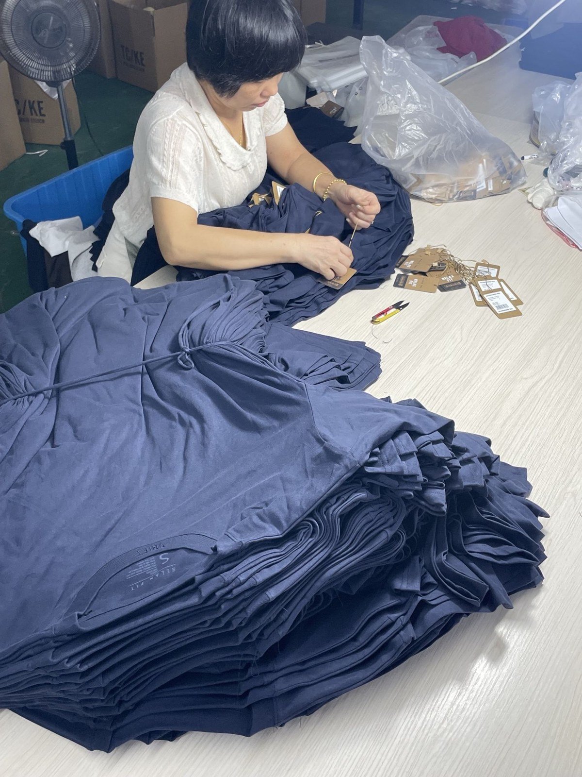 A team member working through a batch of garments at a finishing table.